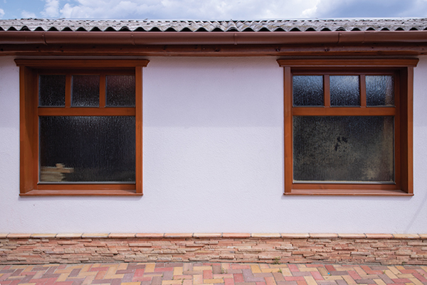 Egy fehér vakolatú családi ház oldalán két fenyő ablakkal.